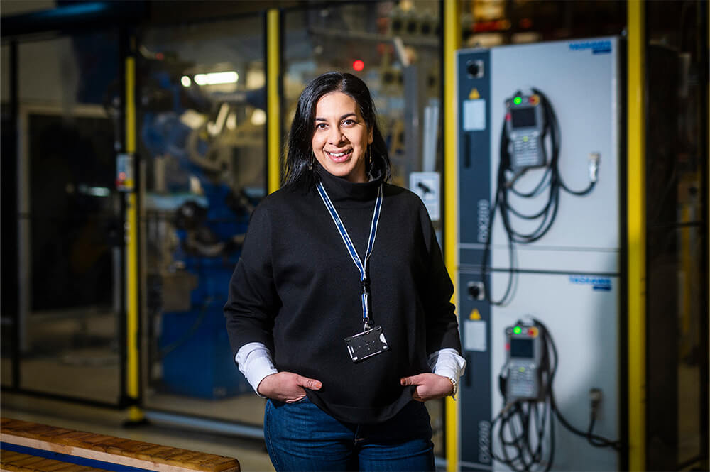 Medarbetare står i en industrimiljö med maskinutrustning i bakgrunden.